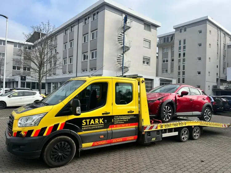 STARK Abschleppdienst Koblenz transportiert beschädigten roten PKW, zuverlässige Hilfe nach einem Unfall in städtischer Umgebung.